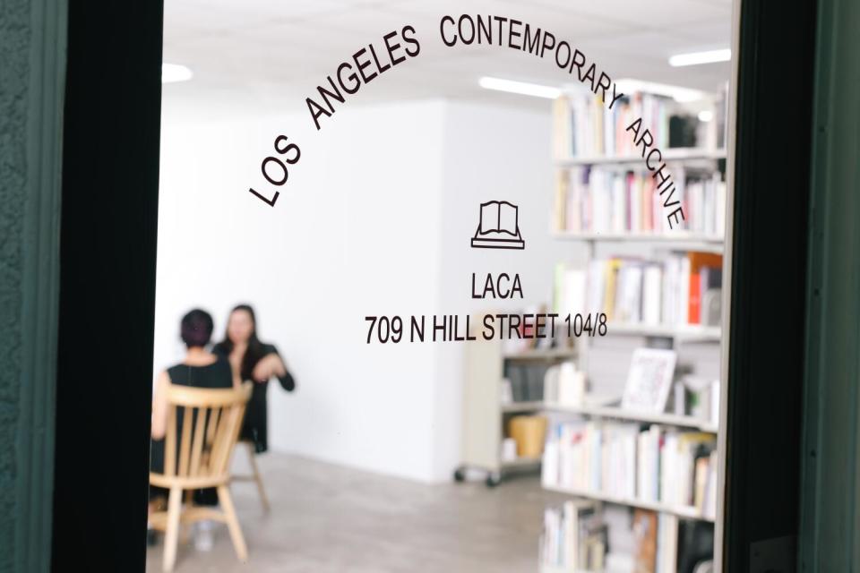 The glass door to Los Angeles Contemporary Archive, through which two seated women are visible.