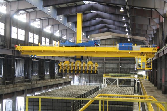 Manufacturing facility with high ceilings and yellow equipment over hundreds of large gray blocks.