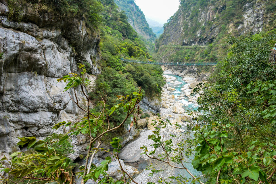 Tourists crossing the bridge over the narrow turquoise Liwu River Gorge surrounded by green mountain valley of Taroko Gorge in Taroko National Park, Xiulin, Hualien, Taiwan