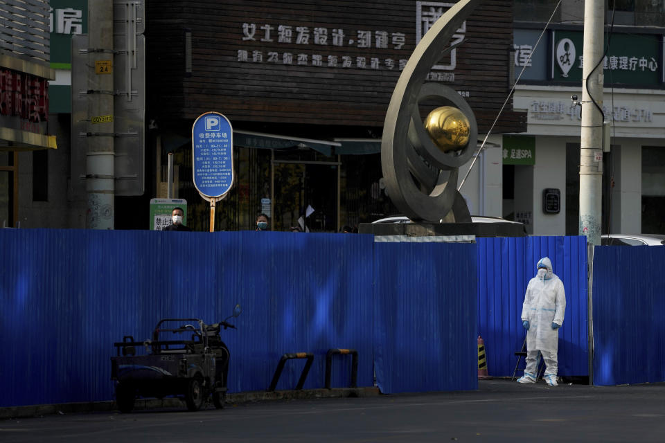 FILE - A worker in protective gear keeps watch as residents gather near metal barriers set up around shuttered shop houses that were locked down as part of COVID-19 controls in Beijing, Nov. 10, 2022. (AP Photo/Andy Wong, File)