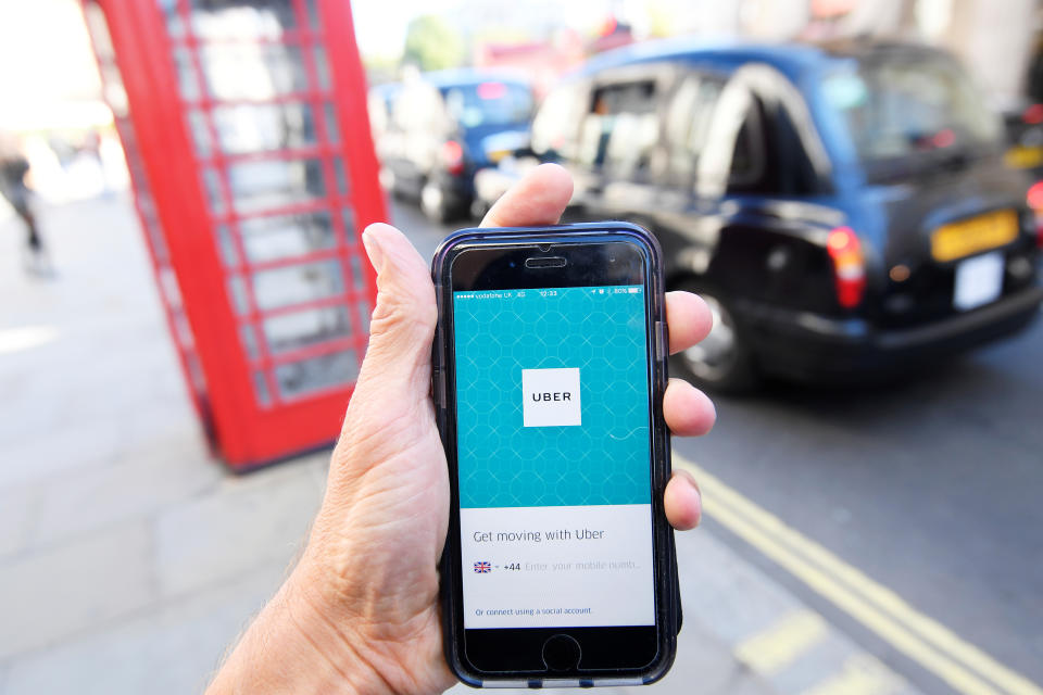 A photo illustration shows a London taxi passing as the Uber app logo is displayed on a mobile telephone, as it is held up for a posed photograph in central London