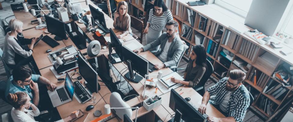 Top view of group of young business people in smart casual wear working together while sitting at the large office desk