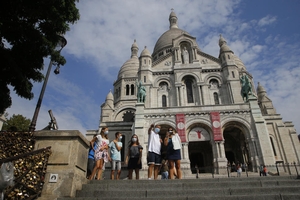 Tourists stroll by the Sacre Coeur basilica in the Montmartre district Monday, Aug. 10, 2020 in Paris. People are required to wear a mask outdoors starting on Monday in the most frequented areas of the French capital. The move comes as the country sees an uptick in virus infections. (AP Photo/Michel Euler)