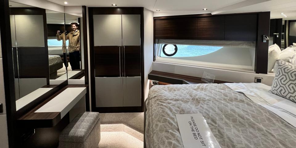 An alternative view of the VIP cabin on a Sunseeker 76 yacht, a wardrobe can be seen next to the window, as well as a mirror and small dressing table, and the bed in grey linen.