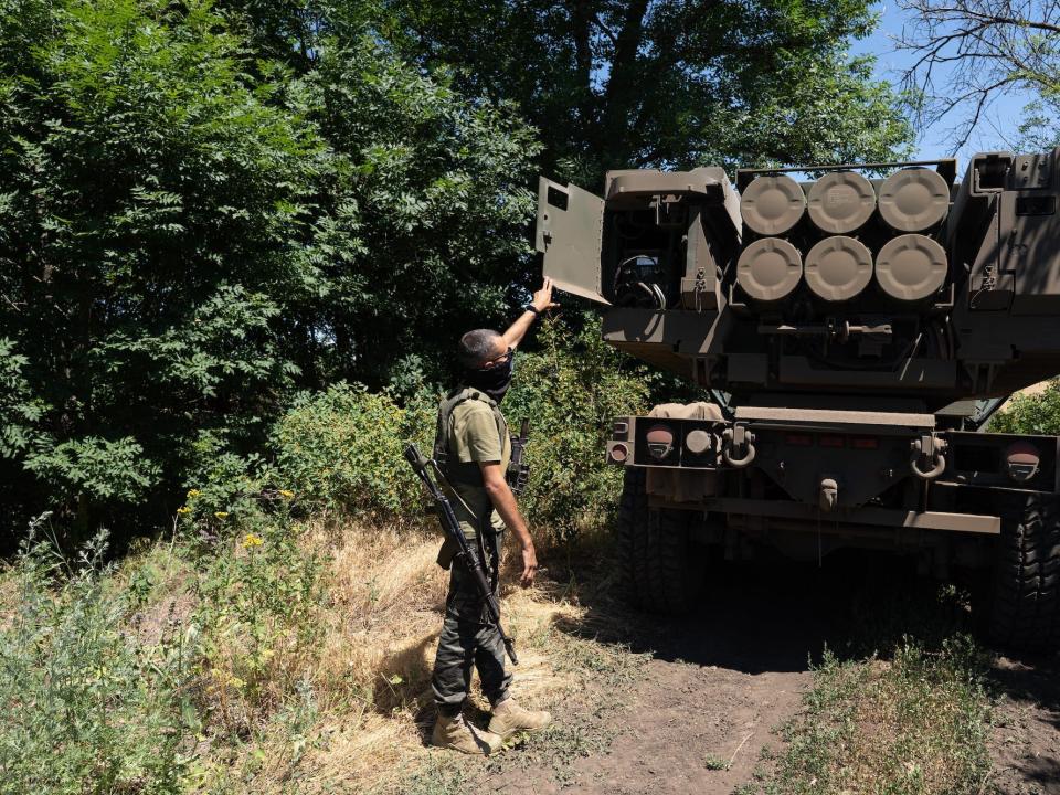 A Ukrainian solider shows the rockets on a HIMARS vehicle between some trees