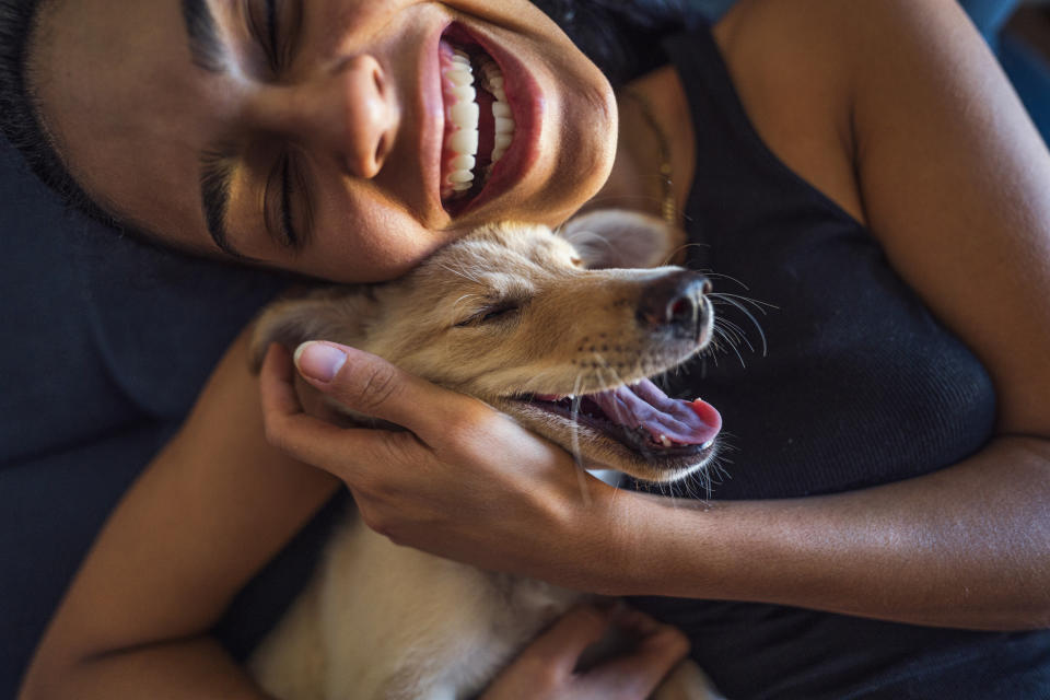 A smiling person in a tank top cuddles a happy puppy close to their face, both looking content and joyful