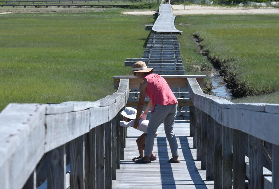 Nicole Holloway holds on tight to her four-year-old daughter Emily peeking through the slats of the Sandwich Boardwalk where it is gated off due to damage from a storm, in a photo from June 2022. Reconstruction of the boardwalk, planned since 2018, could begin as early as the spring, according to town officials.