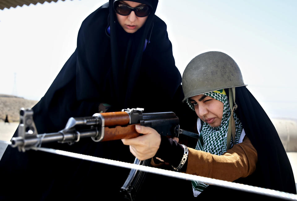 In this Thursday, Aug. 22, 2013 photo, a female member of the Basij paramilitary militia aims a rifle as a trainer looks over her shoulder in Tehran, Iran. With a presence in nearly every city and town across Iran, the paramilitary Basij volunteer corps has an ever-increasing influence on life in the Islamic Republic. (AP Photo/Ebrahim Noroozi)