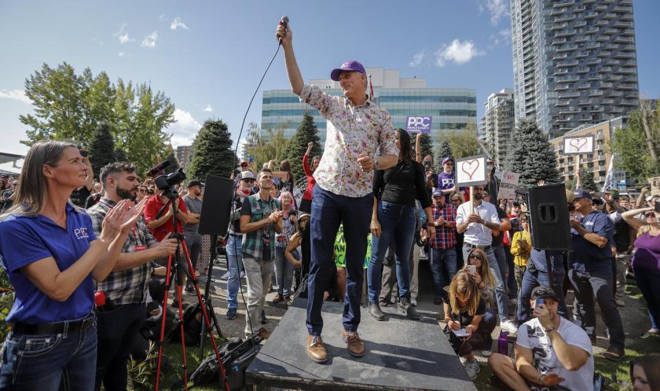 Bernier in a flowered shirt and ball cap appears at a rally surrounded by supporters.