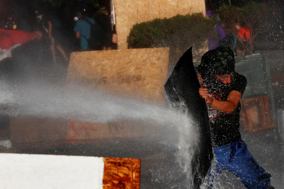 A demonstrator takes cover against a police water cannon during an anti-government protest in Santiago, Chile on Oct. 28, 2019. (Photo: Henry Romero/Reuters)