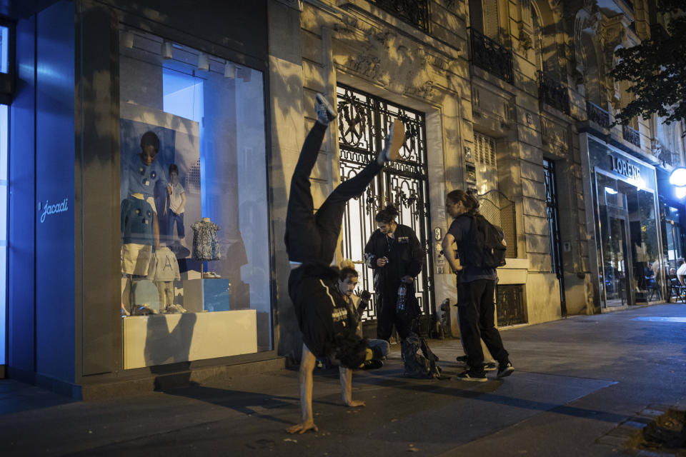 Hadj Benhalima from the collective "On the Spot" makes a headstand during a night of action where they will attempt to extinguish the lights of dozens of storefronts in Paris, Friday, July 29, 2022. (AP Photo/Lewis Joly)