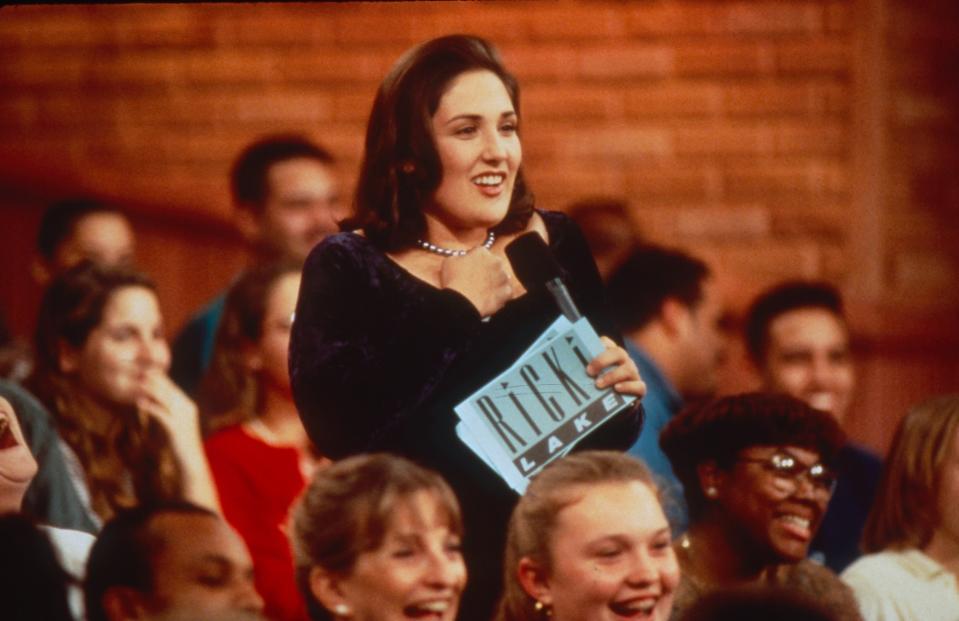 Actress in a velvet dress holding a clapboard among a seated audience