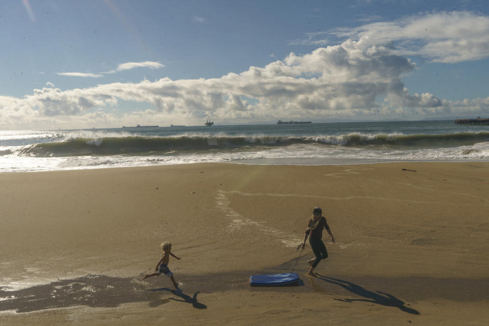 A child runs on the sand with her mother in Seal Beach, Calif., Saturday, Dec. 30, 2023. (AP Photo/Damian Dovarganes)