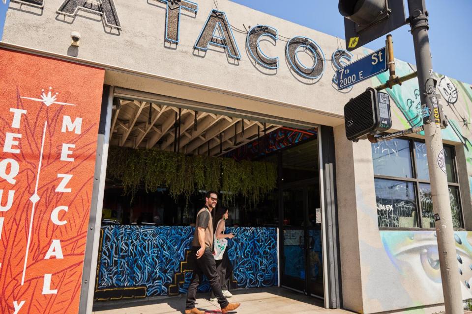 A man and a woman walk into a restaurant with paintings on the exterior.