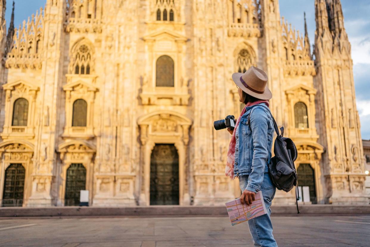 Beautiful young female tourist taking  a picture of the cathedral in Milan, Italy, using camera.