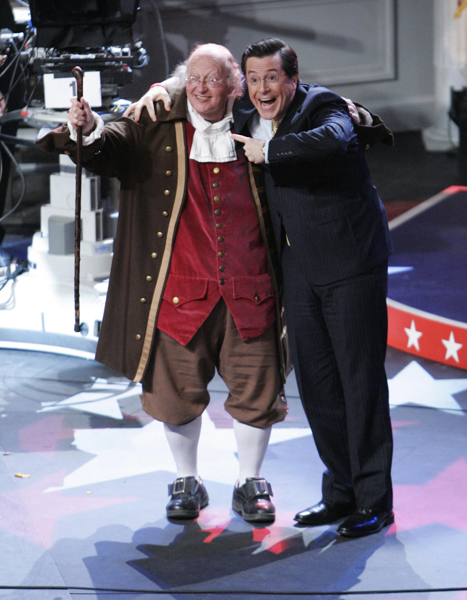FILE – In this April 17, 2008, file photo, television host Stephen Colbert, right, of Comedy Central's "The Colbert Report" points at re-enactor Ralph Archbold, left, portraying Benjamin Franklin, after the recording of the program at the University of Pennsylvania in Philadelphia. Archbold, who portrayed Franklin in Philadelphia for more than 40 years, died Saturday, March 25, 2017, at age 75, according to the Alleva Funeral Home in Paoli, Pa. (AP Photo/Matt Rourke, File)