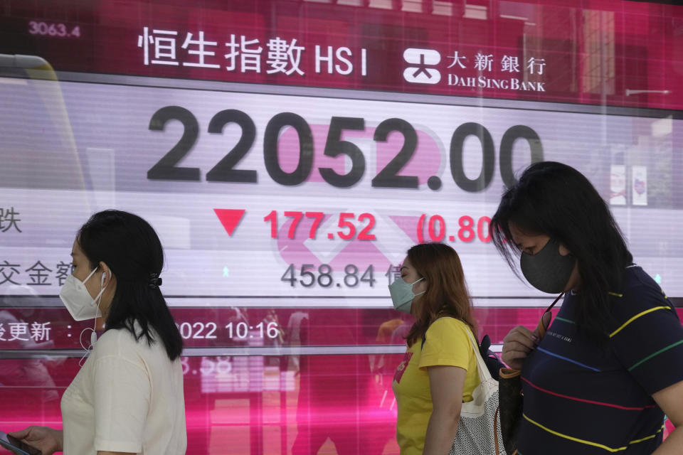 People wearing face masks walk past a bank's electronic board showing the Hong Kong share index in Hong Kong, Tuesday, June 28, 2022. Asian shares were mixed Tuesday after a wobbly day on Wall Street as markets cooled off following a rare winning week. (AP Photo/Kin Cheung)