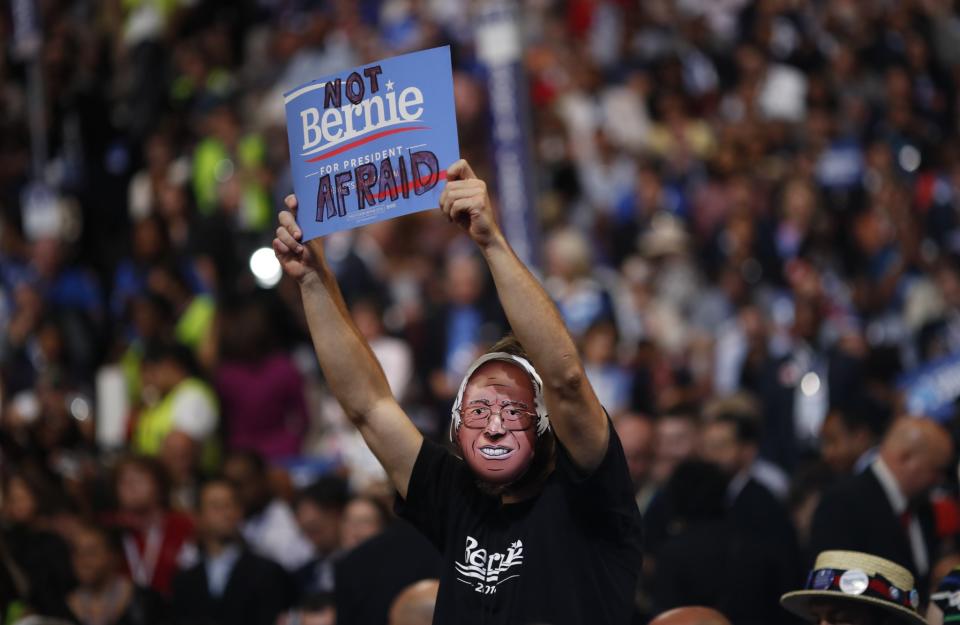 A delegate wearing a Bernie Sanders T-shirt and mask holds up a sign on the third night at the Democratic National Convention in Philadelphia on July 27, 2016. (Photo: Carlos Barria/Reuters)