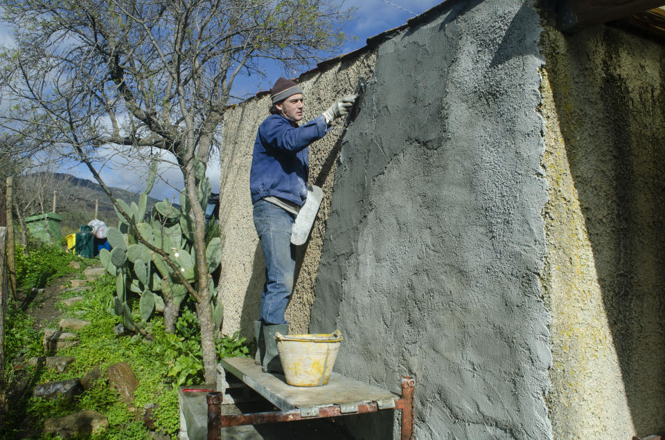 This image provided by Audrey Rodeman shows Cain Burdeau covering a wall of a small concrete house where he lives with his family outside Castelbuono, Sicily, Italy, in a coat of concrete plaster. Burdeau had to become familiar with masonry to build in Italy, a land where laborers have long excelled with trowels, chisels, mortar mixes, stones and bricks. (Audrey Rodeman via AP)