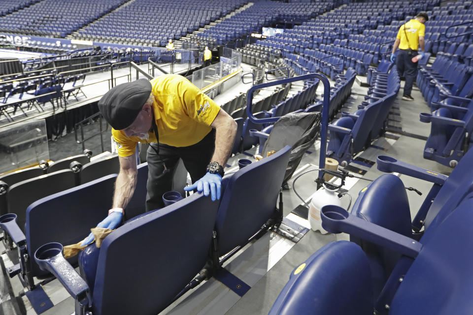 Luis Rivera, left, sanitizes seats in Bridgestone Arena after the remaining NCAA college basketball games in the Southeastern Conference tournament were cancelled Thursday, March 12, 2020, in Nashville, Tenn. The tournament was cancelled Thursday due to coronavirus concerns. (AP Photo/Mark Humphrey)