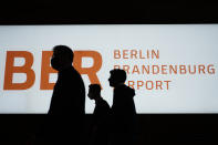 People walk in front of a sign of the new Berlin-Brandenburg-Airport 'Willy Brandt' in inside the Terminal 1, near Berlin in Schoenefeld, Germany, Tuesday, Oct. 27, 2020. After years of delays and massive cost overruns the opening of the German capital's new airport is scheduled for Saturday Oct. 31.(AP Photo/Markus Schreiber)