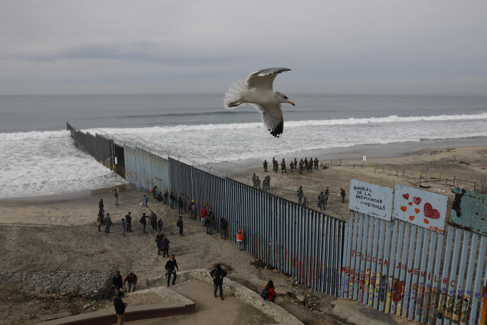 FILE - In this Dec. 10, 2018, file photo, people look on from the Mexican side, left, as U.S. Border Patrol agents on the other side of the U.S. border wall in San Diego prepare for the arrival of hundreds of pro-migration protestors, seen from Tijuana, Mexico. A relentless stream of U.S. policy shifts in 2018 has amounted to one of the boldest attacks on all types of immigration that the country has ever seen. Some see it as a tug-of-war between foundational national ideals and a fight for a new path forward led by President Donald Trump. (AP Photo/Rebecca Blackwell, File)