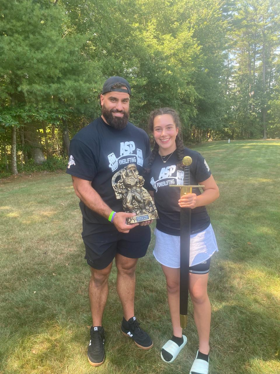 Braintree High sophomore powerlifter Bella Duffy holds the sword she won at a competition over the summer. On the left is her coach, Rob Ruggiero of Atlantic Sports Performance in Hanover.