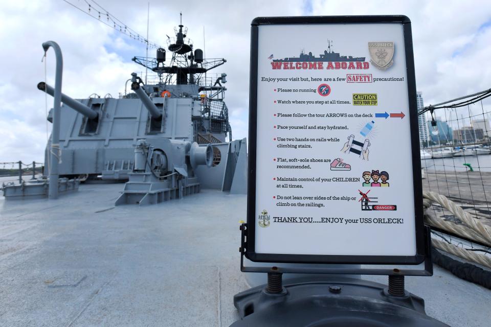 A sign welcomes visitors to the Orleck and reminds them to follow safety procedures while aboard the floating naval museum. In the background is the ship's 5-inch, 38-caliber gun turret.