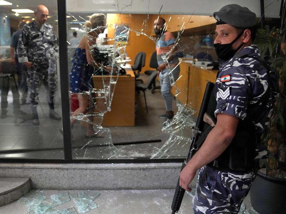 A Lebanese policeman stands guard next to a bank window that was broken by depositors to exit the bank after attacking it trying to get their money, in Beirut, Lebanon, Wednesday, Sept. 14, 2022.