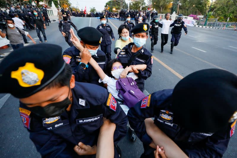 A pro-democracy protester flashes the three-finger salute while she is detained by police officers in front of the Government House during a rally in Bangkok