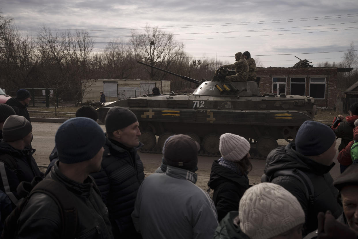 Residents lining up for aid watch as Ukrainian soldiers ride atop a tank in the town of Trostsyanets, Ukraine, Monday, March 28, 2022. Trostsyanets was recently retaken by Ukrainian forces after being held by Russians since the early days of the war. (AP Photo/Felipe Dana)