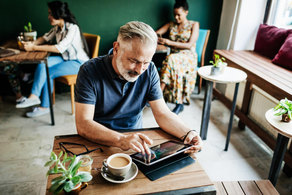 A mature man using a digital table in a cafe while he relaxes with a cup of coffee.