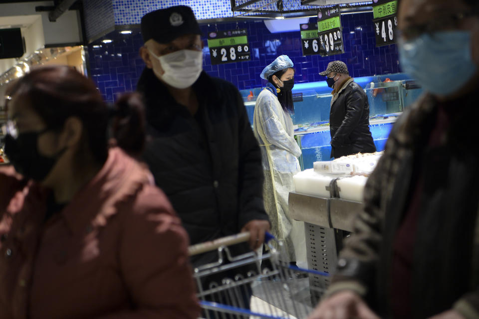 A masked woman wearing a raincoat and cover her head with a plastic bag shops for food with others at a supermarket in Wuhan in central China's Hubei province, Monday, Feb. 10, 2020. China reported a rise in new virus cases on Monday, possibly denting optimism that its disease control measures like isolating major cities might be working, while Japan reported dozens of new cases aboard a quarantined cruise ship. (Chinatopix via AP)