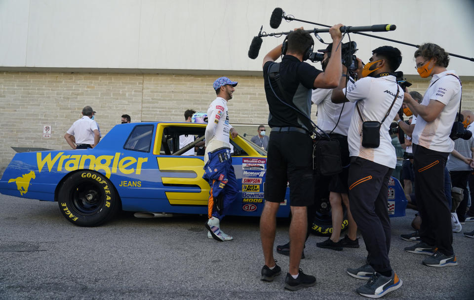 McLaren driver Daniel Ricciardo, of Australia, left, talks to media as he prepares to drive the late Dale Earnhardt's iconic 1984 No. 3 Wrangler Chevrolet Monte Carlo before an open practice for the Formula One U.S. Grand Prix auto race at the Circuit of the Americas, Saturday, Oct. 23, 2021, in Austin, Texas. Ricciardo was allowed to drive the car as a reward from his McLaren boss, Zak Brown, for winning his first race with the team. (AP Photo/Eric Gay)