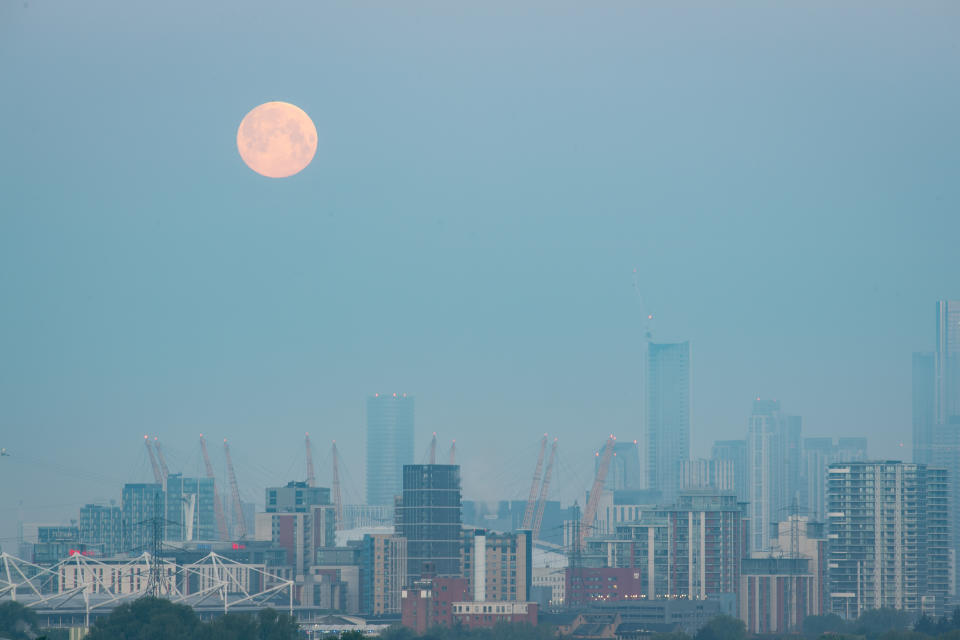 The moon sets over The O2 Arena and tall buildings in east London.