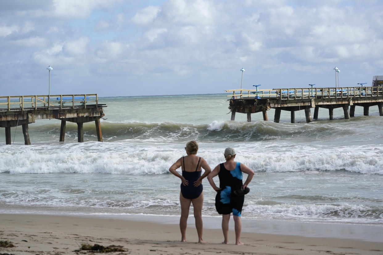 Two women in bathing suits look at a substantial gap in the pier.