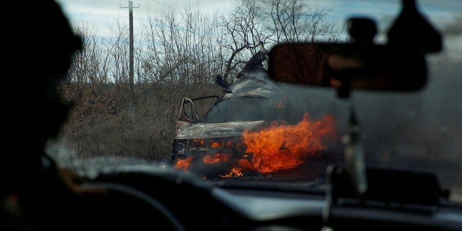 Ukrainian soldiers drive past a burning car
