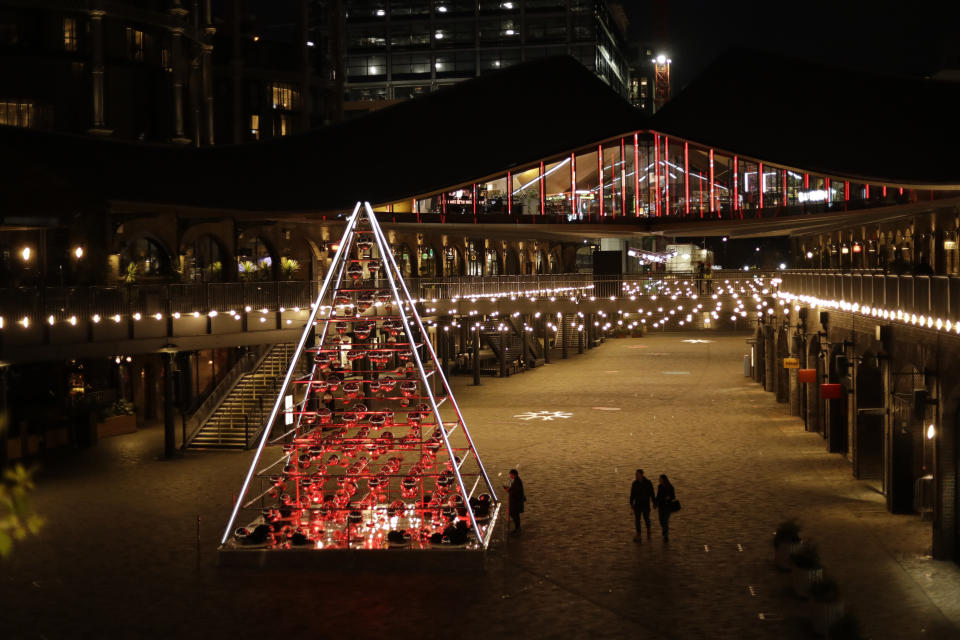 FILE - In this Monday, Nov. 23, 2020 file photo, people walk past the 'Terrarium Tree' in Coal Drops Yard, which forms part of the King's Cross neighbourhood of London's unconventional Christmas tree installations, during England's second coronavirus lockdown. Nations are struggling to reconcile cold medical advice with a holiday tradition that calls for big gatherings in often poorly ventilated rooms, where people chat, shout and sing together, providing an ideal conduit for a virus that has killed over 350,000 people in Europe so far. (AP Photo/Matt Dunham, FIle)