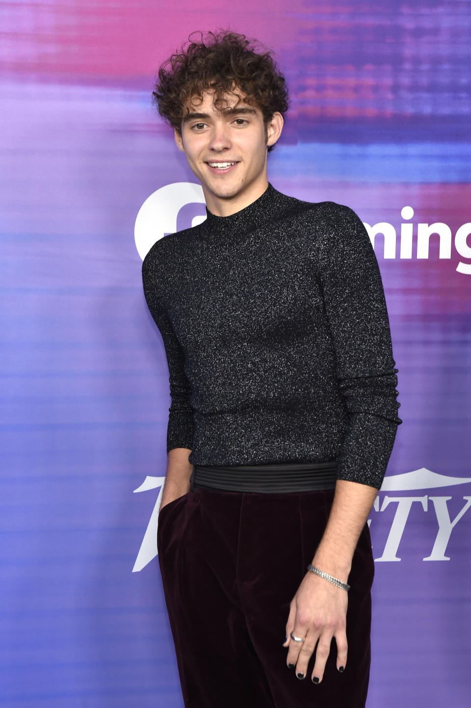 Joshua smiling on the red carpet in a sparkling top and nail polish