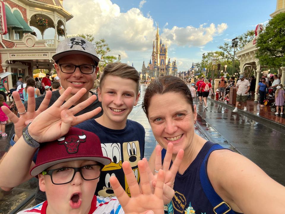 kari and her family posing holding up four fingers in front of cinderella castle at disney world