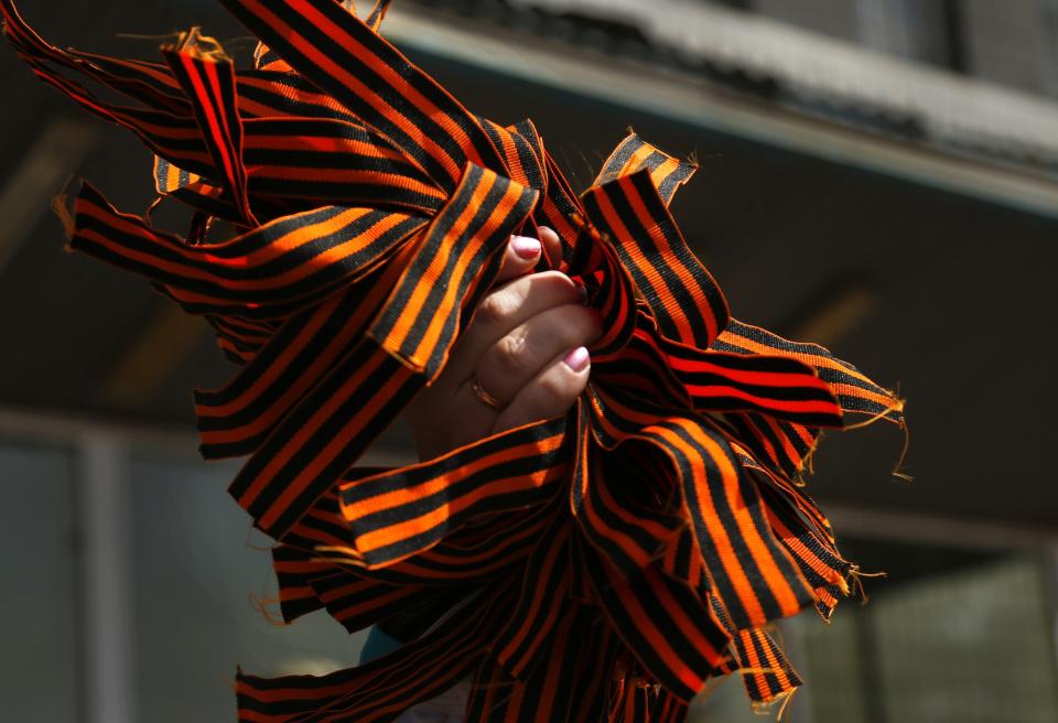 FILE - In this Monday, April 28, 2014 file photo, a pro Russian activist distributes St. George ribbons to militants at the city hall in Kostyantynivka, 35 kilometers (22 miles) south of Slovyansk, eastern Ukraine, after masked militants with automatic weapons seized the hall building. The propaganda assault began during the pro-Western Maidan protests late last year that ousted Ukraine’s pro-Russian president in February: Russian state news media were quick to dismiss the protests as the work of Ukrainian neo-Nazis, a particularly loaded accusation because Ukrainian nationalists collaborating with the Nazis are blamed for horrific reprisal attacks during World War II. (AP Photo/Sergei Grits, File)