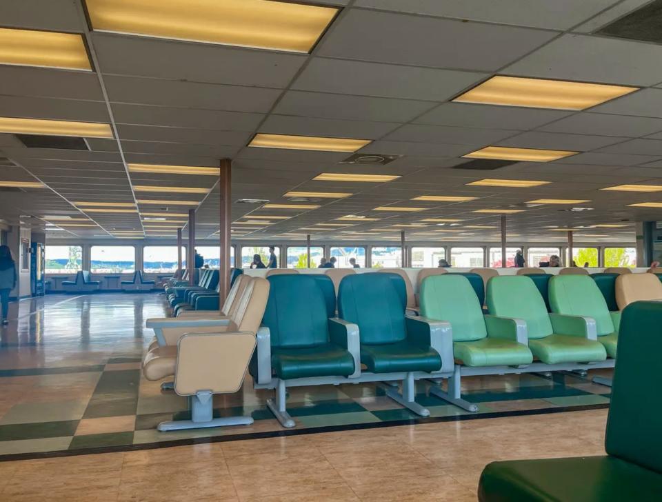 Several tan, dark-green, and light-green seats on a ferry with fluorescent lights and low ceilings