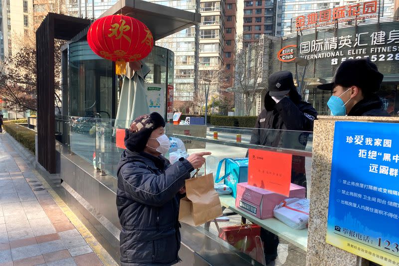 Delivery man passes a bag over the wall at a residential compound as the country is hit by an epidemic of the new coronavirus, in Beijing