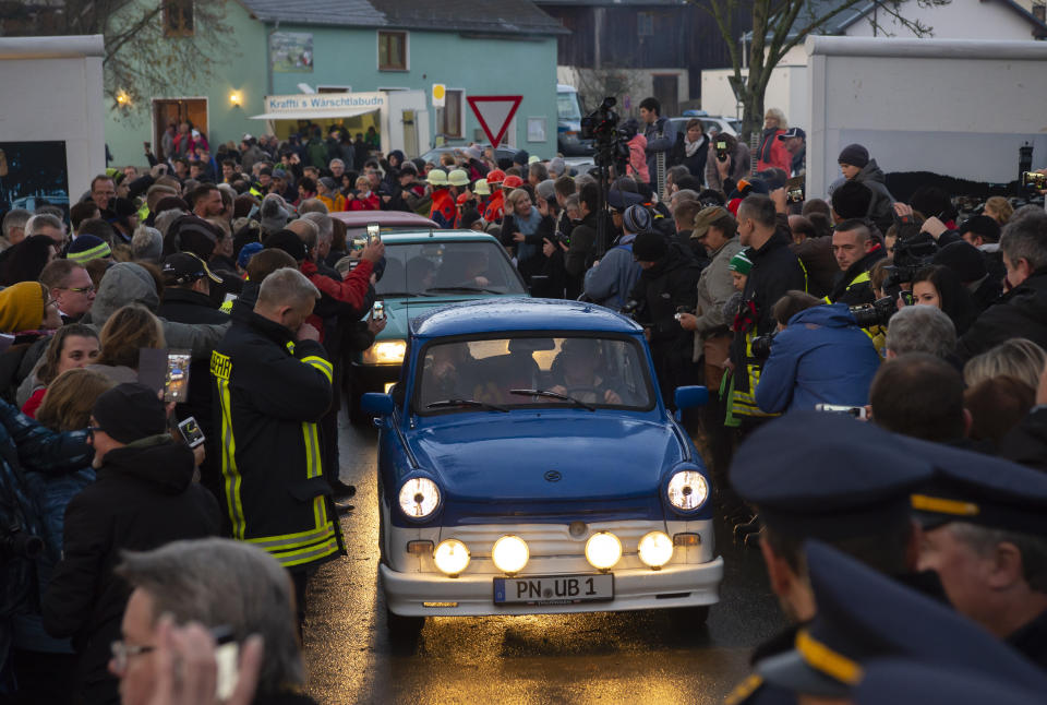 People welcome the legendary GDR Trabant (Trabi) cars, during a symbolic wall opening, celebrating the 30th anniversary of the falling wall in the outdoor area of the German-German museum in Moedlareuth, Germany, Saturday, Nov. 9, 2019. Moedlareuth, named 'Little Berlin', was the symbol of a divided village along the borderline between East and West Germany. The border ran straight through the little village. (AP Photo/Jens Meyer)