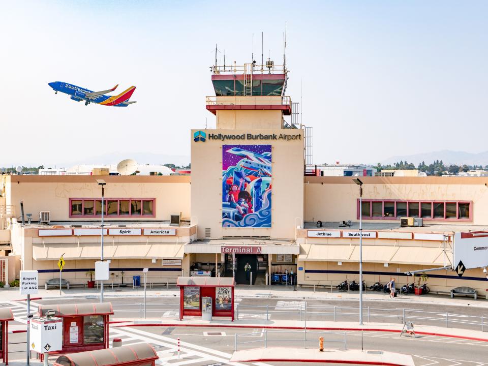 The exterior of Hollywood Burbank Airport's terminal building with a plane taking off in the background.