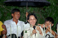 FILE - An aid holds an umbrella over Burmese democratic leader Aung San Suu Kyi during her daily appearance at the gate of her Yangon (formerly known as Rangoon) home from where she greets a crowd of supporters that gathered in the street on July 16, 1995. Myanmar court on Monday, Dec. 6, 2021, sentenced ousted leader Suu Kyi to 4 years for incitement and breaking virus restrictions, then later in the day state TV announced that the country's military leader reduced the sentence by two years. (AP Photo/Anat Givon, File)