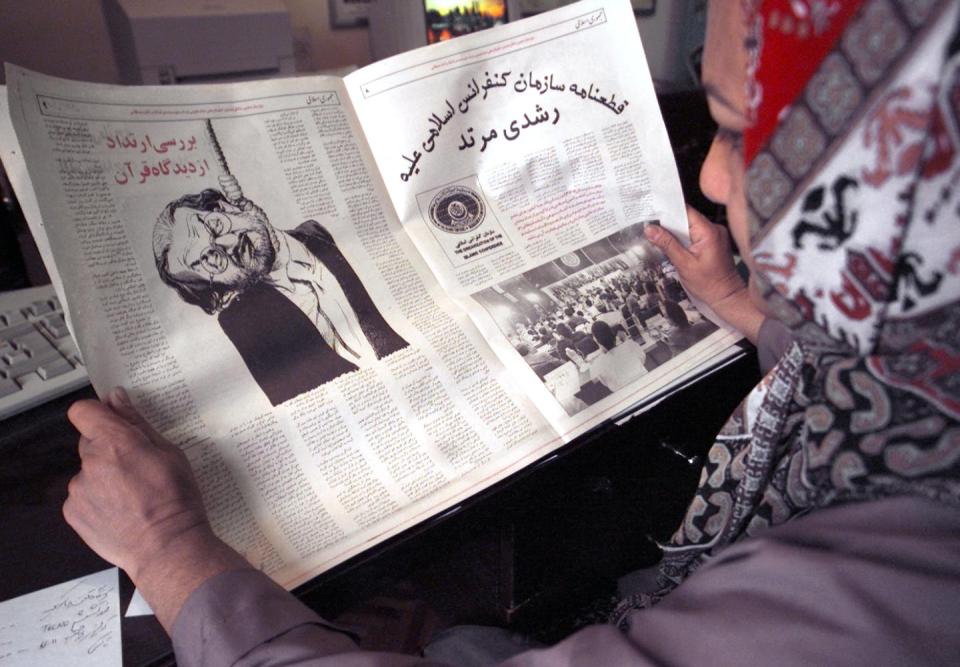 An Iranian woman reads a newspaper in 2000 with a drawing depicting British author Salman Rushdie as a hanged man. <a href="https://www.gettyimages.com/detail/news-photo/an-iranian-woman-reads-a-paper-in-tehran-14-february-2000-news-photo/1242459432?adppopup=true" rel="nofollow noopener" target="_blank" data-ylk="slk:Henghameh Fahimi/AFP via Getty Images;elm:context_link;itc:0;sec:content-canvas" class="link ">Henghameh Fahimi/AFP via Getty Images</a>
