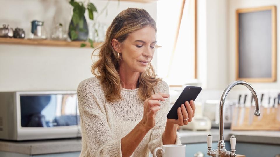 A blonde woman holding her cell phone in a kitchen, which hampers vision