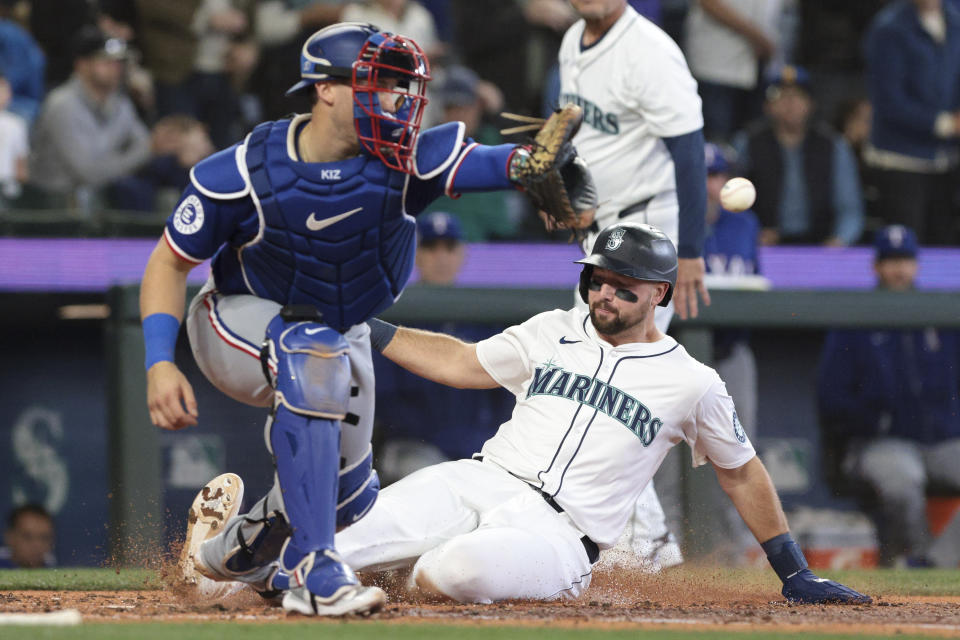 Seattle Mariners' Cal Raleigh, right, beats the throw to Texas Rangers catcher Andrew Knizner to score during the third inning of a baseball game Saturday, June 15, 2024, in Seattle. (AP Photo/Jason Redmond)