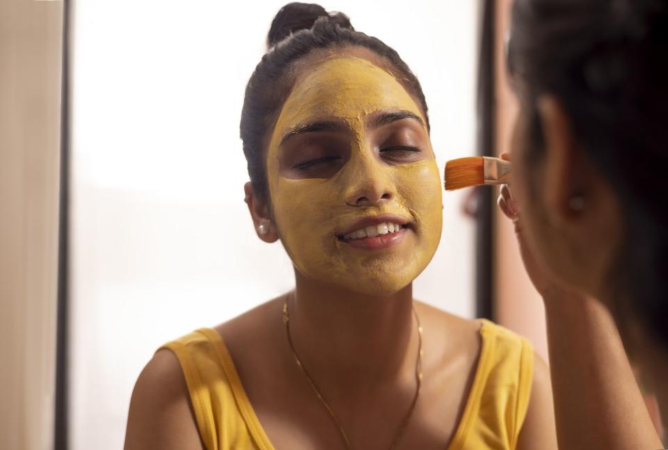 woman applying turmeric face pack on her friend's face